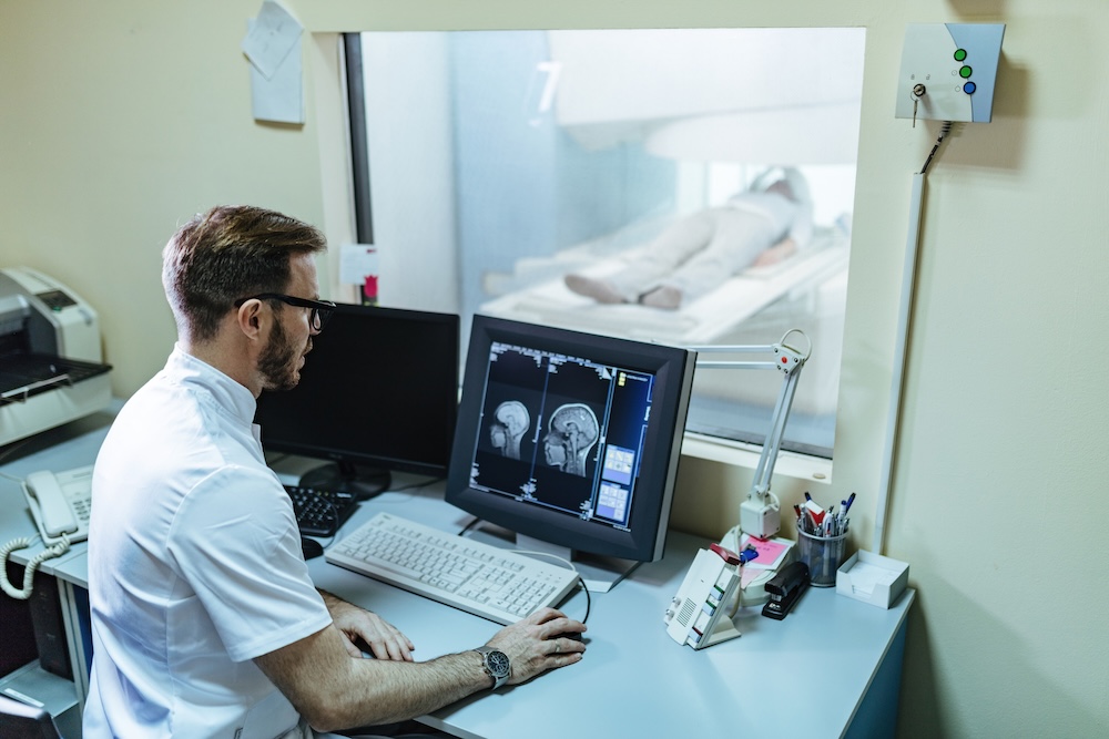 Doctor supervising brain scan procedure of a patient from control room.